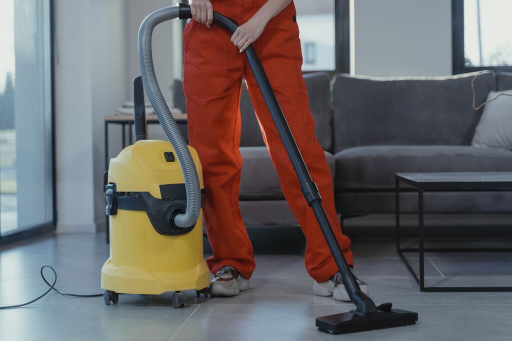 Professional cleaner in coveralls vacuuming the floor of an apartment unit